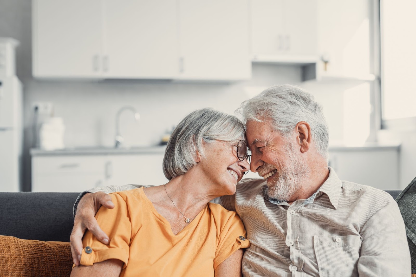 Older husband has his arm around his wife, their foreheads pressed together after talking about managing dementia.