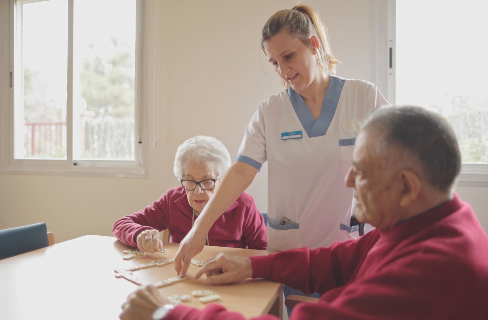 Caregiver helping elderly residents with cognitive activities, emphasizing specialized care and engagement for individuals with memory-related conditions.