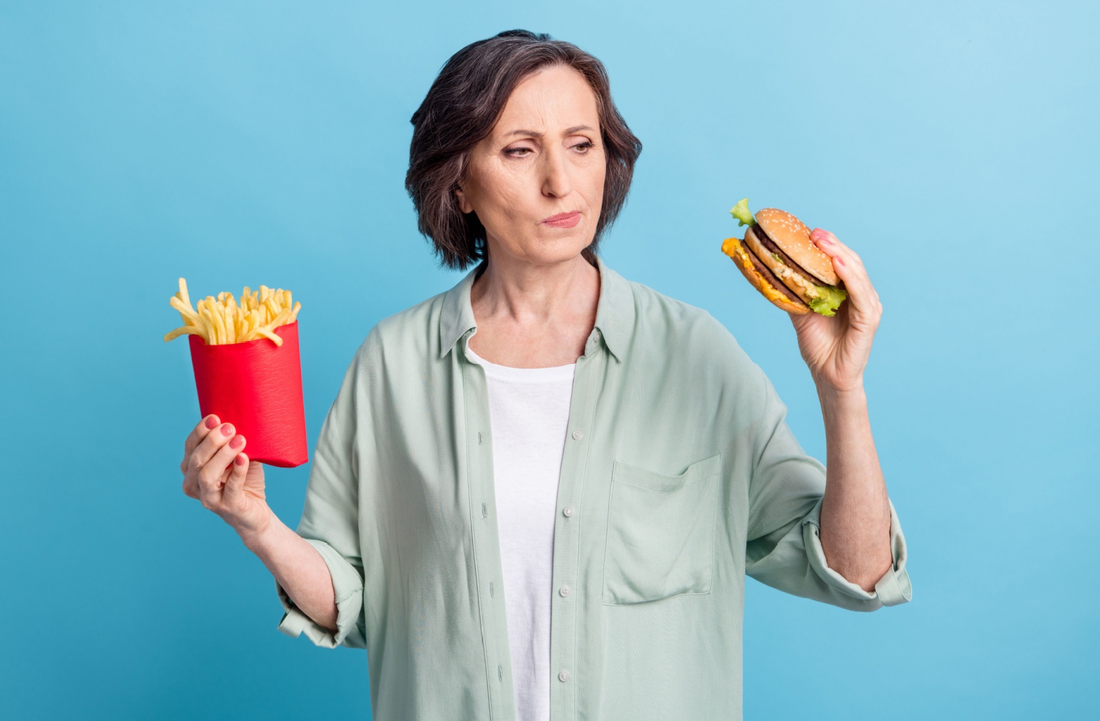 An older person considers the fast food burger and fries they're holding.