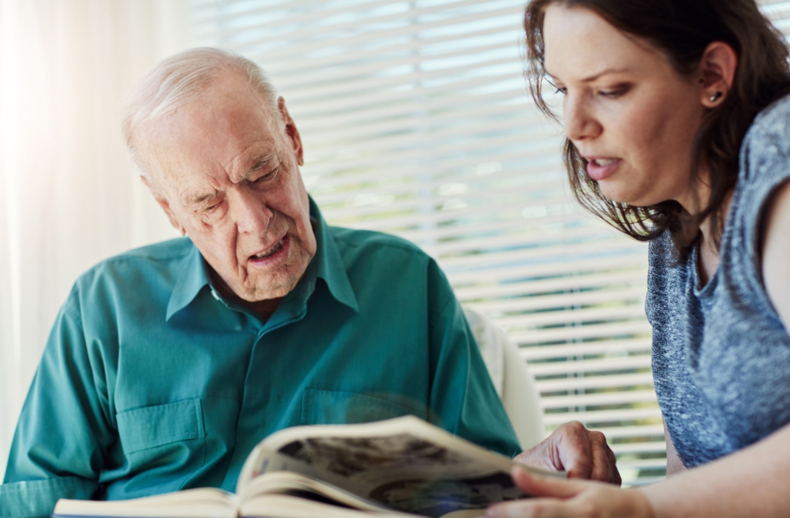 Elderly man with dementia looking through a photo album with a caregiver.