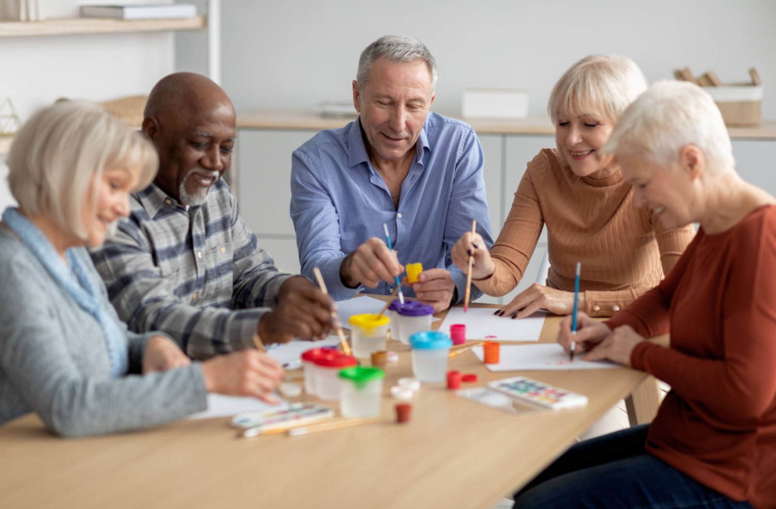 Group of older adults painting and enjoying an art activity together at a table.