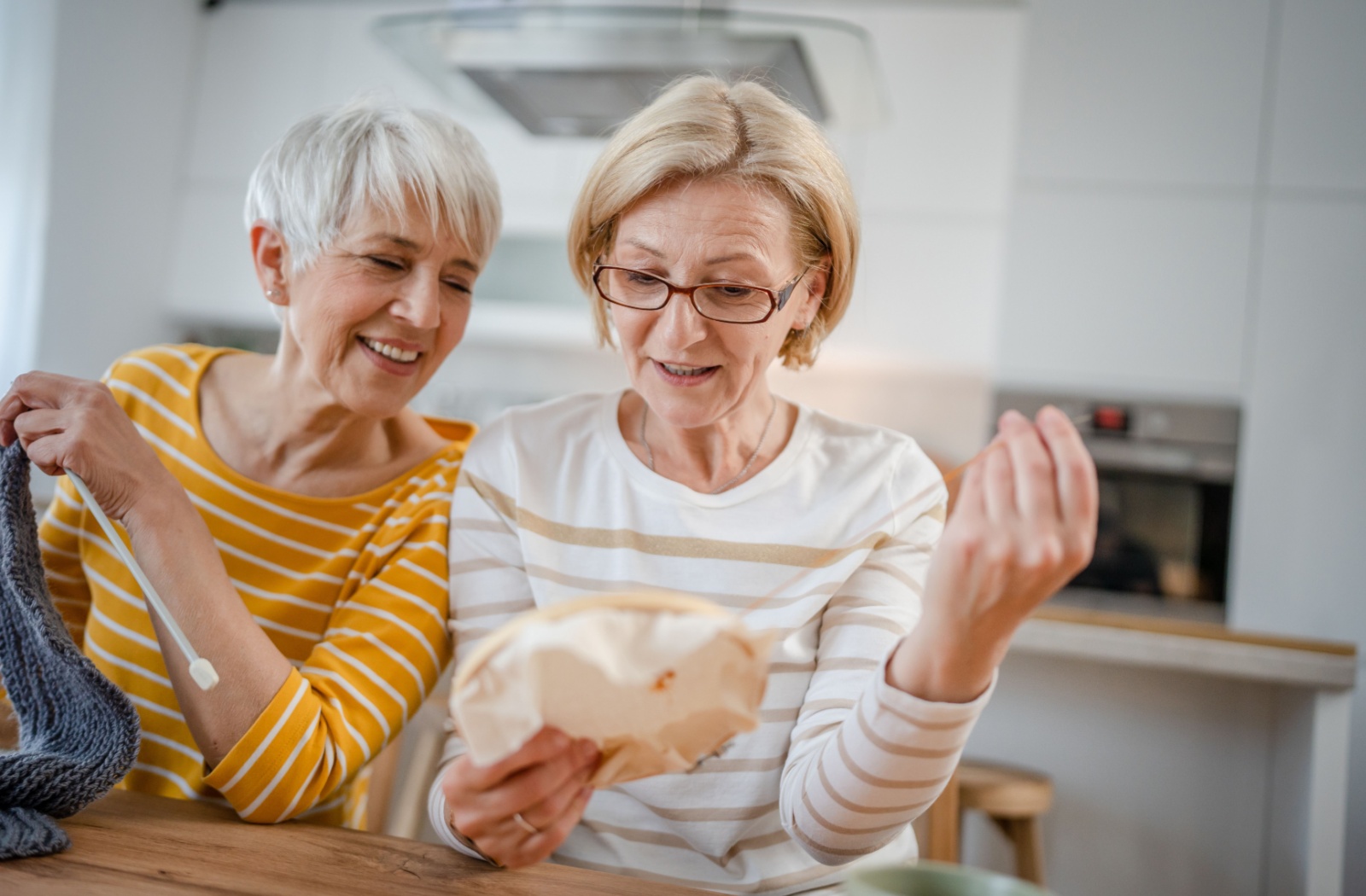 A pair of older adults laughing while knitting and embroidering together in an arts class.