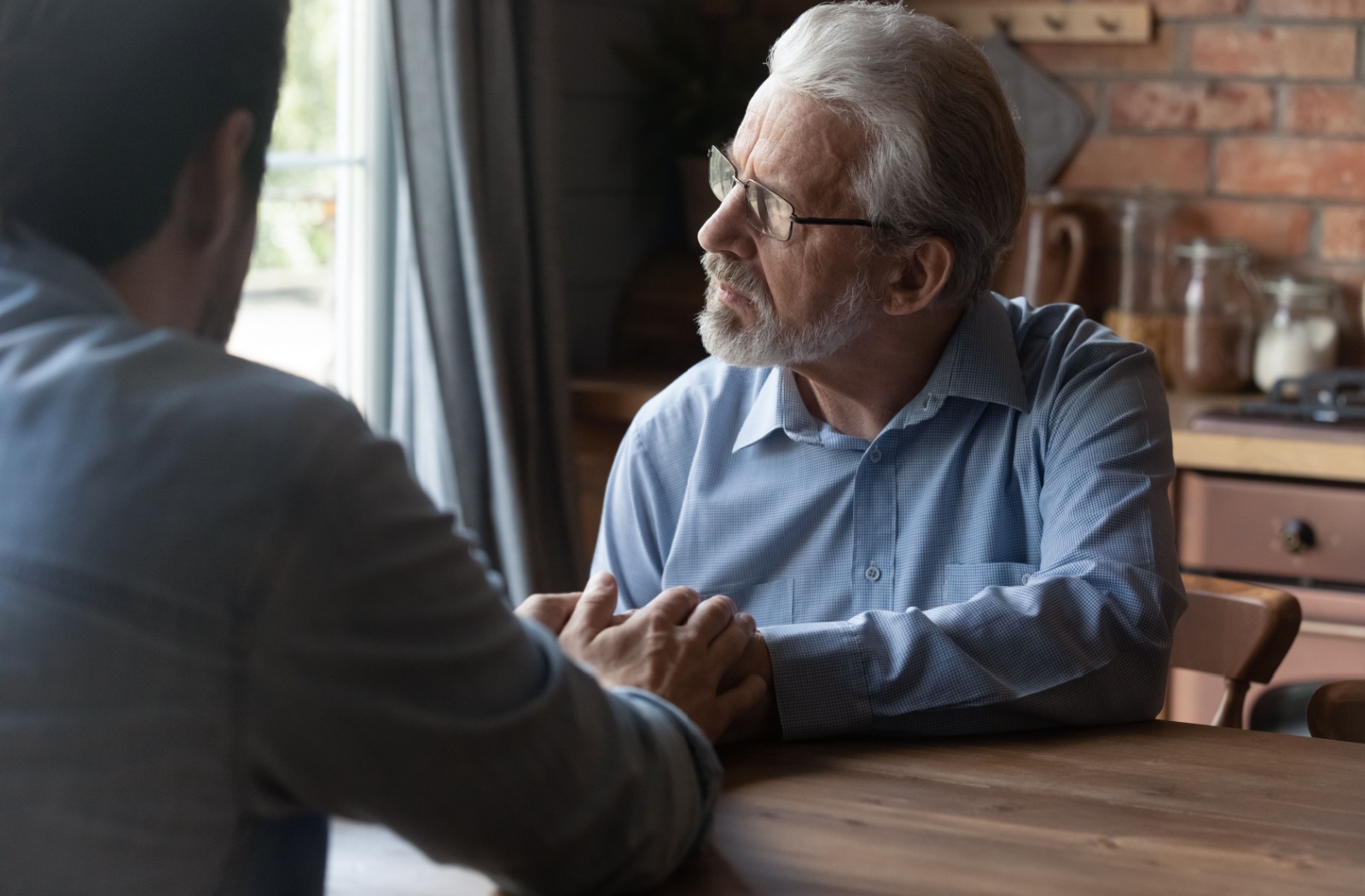 An older adult looking out the window, deep in thought, while talking to their adult child about memory loss.
