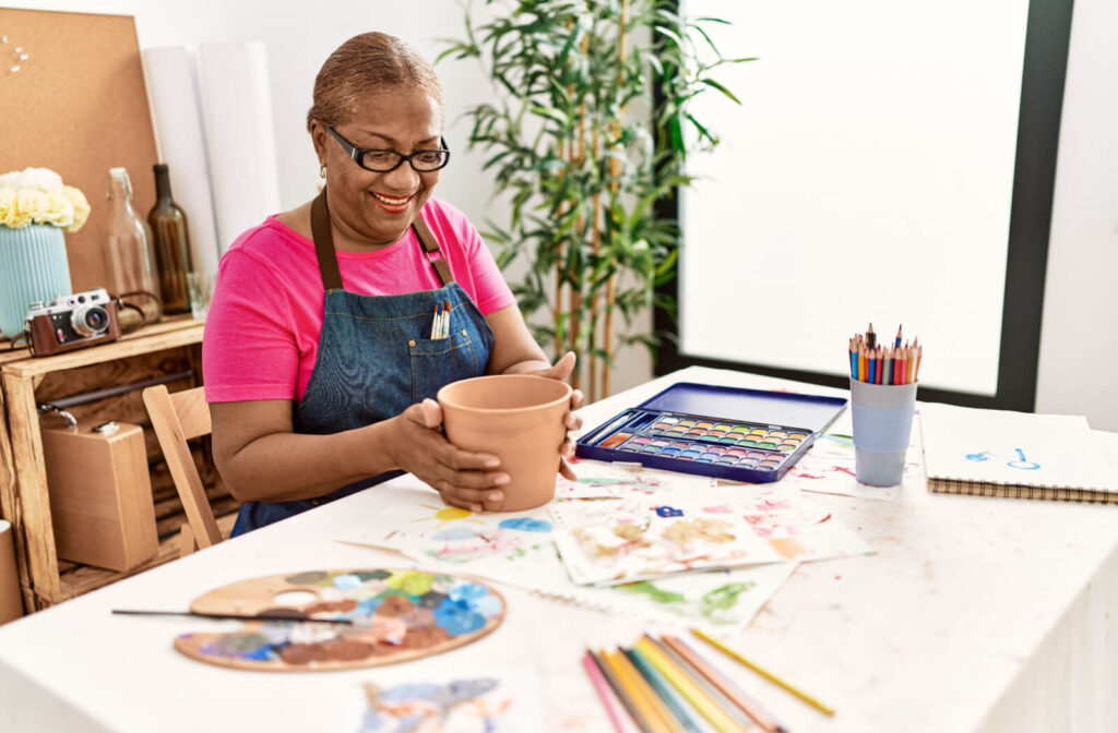 An older adult grinning while preparing a clay pot to paint with watercolors.
