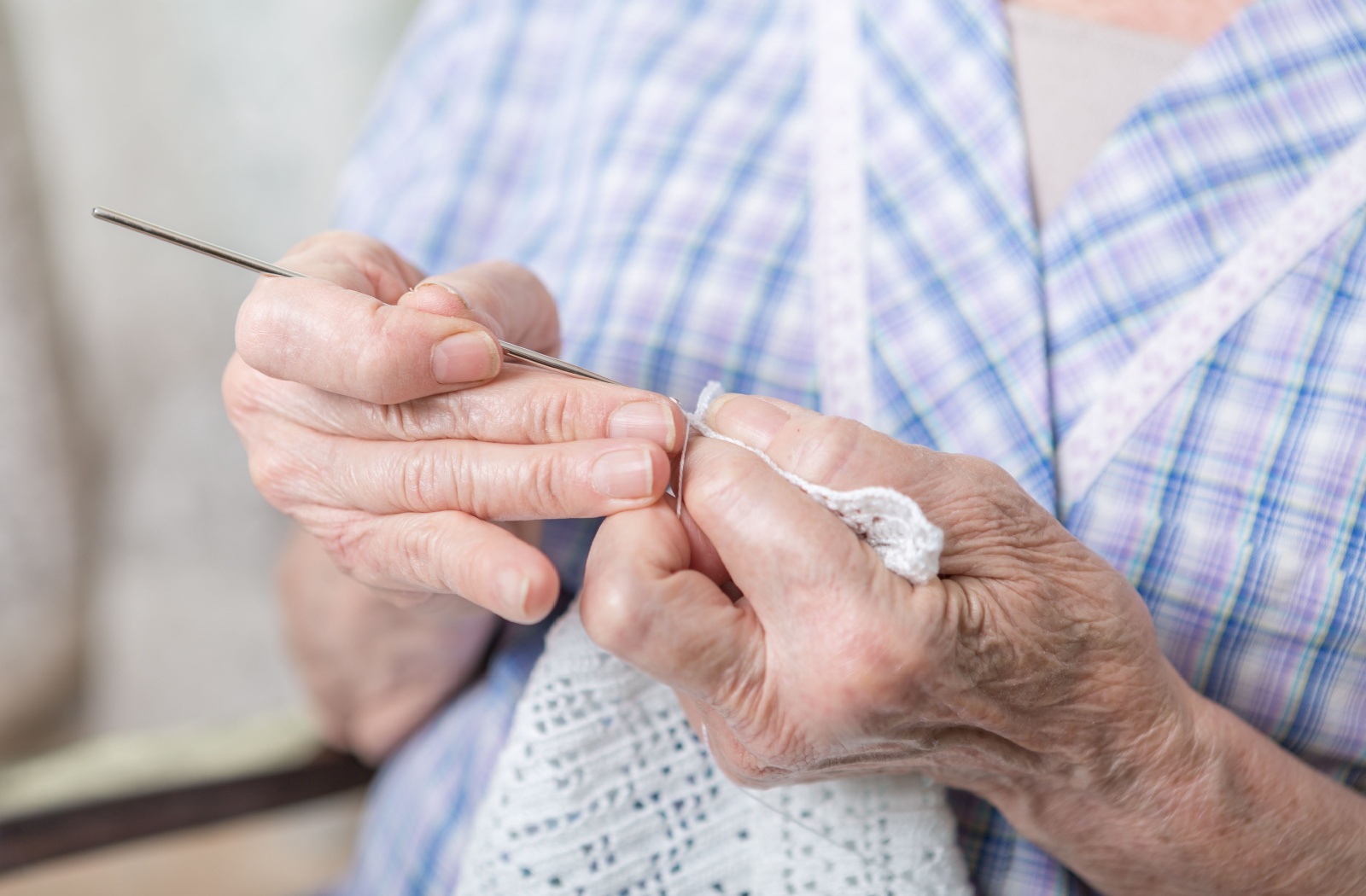 A close-up image of an older adult carefully crocheting a white hankerchief to train their memory