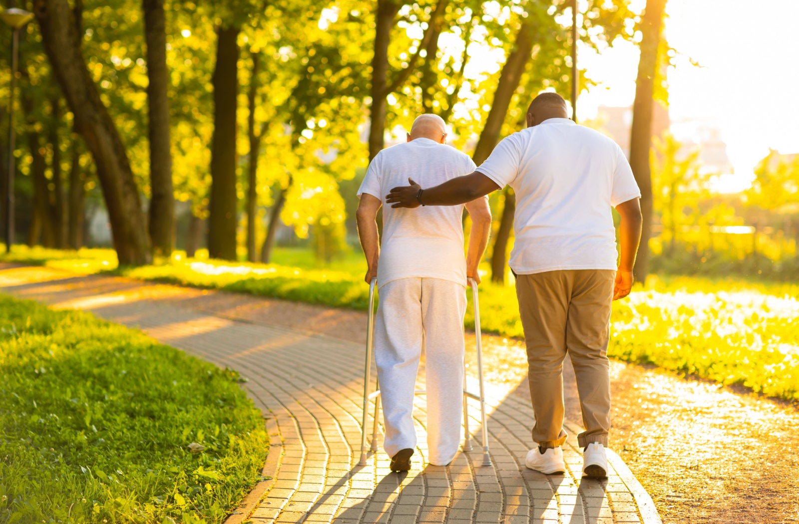 A senior living caregiver helps a senior with a walker take a walk outside to promote movement and enjoy fresh air
