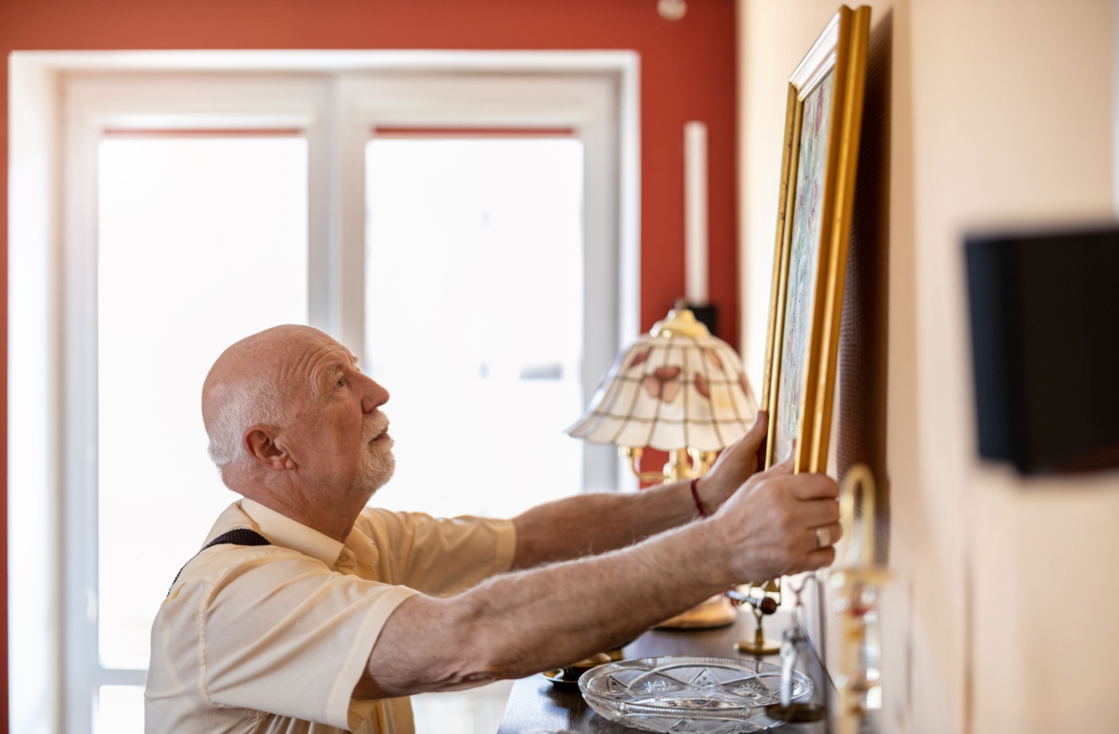 A senior with dementia hangs a well-loved framed painting in their memory care home so it can create a sense of familiarity